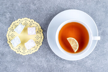 Cup of tea with lemon and soft candies on marble surface