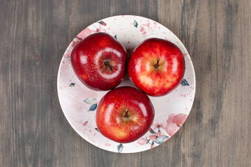 A white plate with red juicy apples on a wooden table