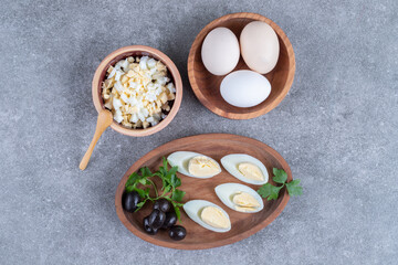 A wooden board with olives and boiled eggs