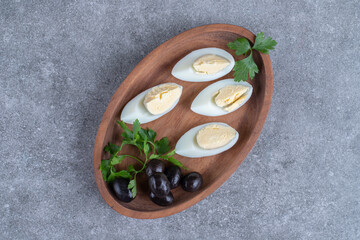 A wooden board with olives and boiled eggs