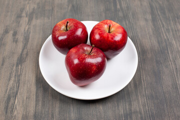 A white plate with red juicy apples on a wooden table