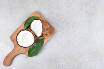 A wooden cutting board with sliced coconut and leaves