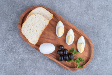 A wooden cutting board with boiled egg and slices of bread