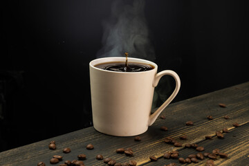 A mug of hot coffee with evaporation and steam and a small splash on a wooden table against a dark background