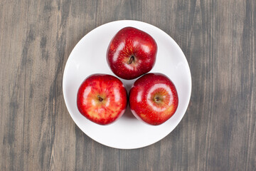 A white plate with red juicy apples on a wooden table