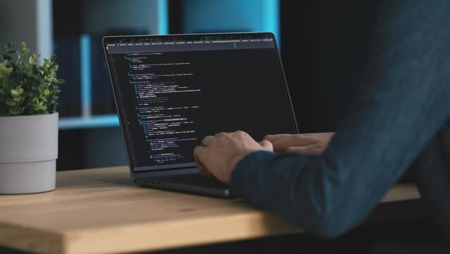 Man coding software at laptop, coder in dark office writing code