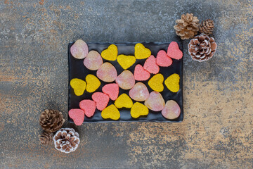A dark plate full of heart shaped sugary jelly candies with pinecones