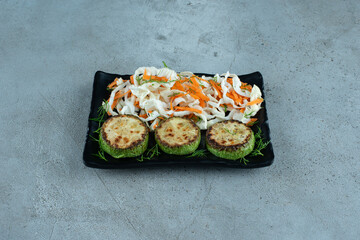 Chopped cabbage and carrots with grilled pepper on black plate