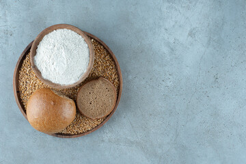 Rye bun with bowl of flour on wooden plate