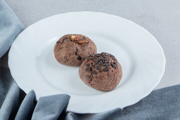 Chocolate chip cookies on a white platter next to table cloth on marble background