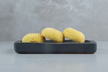 Yellow cookies on a black tray on marble background