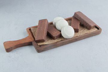 Chocolate wafers and cookies bundled on a wooden tray on marble background