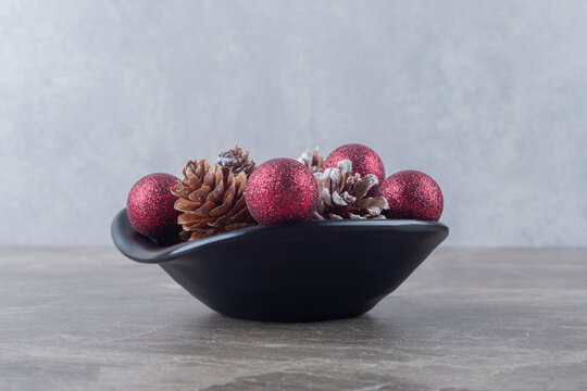 Bundle Of Pine Cones And Christmas Baubles In A Bowl On Marble Background