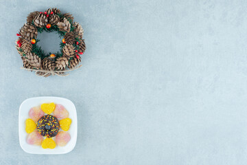 Pine cone wreath and a platter of marmelades and a donut on marble background