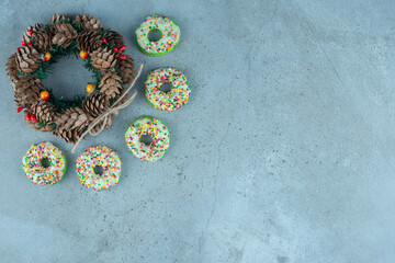 Small donuts around a pine cone wreath on marble background