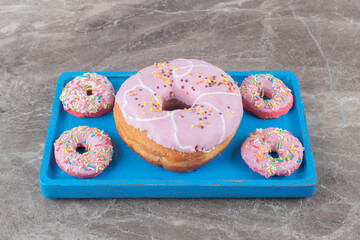 Large and small donuts arranged on a blue platter on marble background