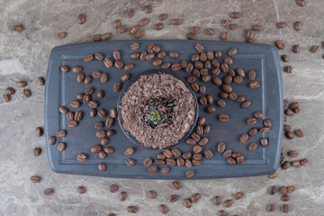 Chocolate coated cake and coffee beans on a navy board on marble background