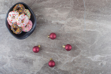 Bowl of donuts and christmas baubles on marble background