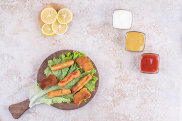 Grilled sausages with chicken nuggets on a piece of lettuce on a wooden board with sauces aside