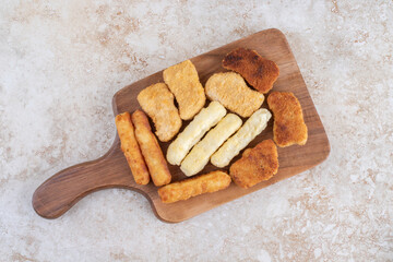 Classic chicken nuggets, sausage and cheese sticks on a wooden platter