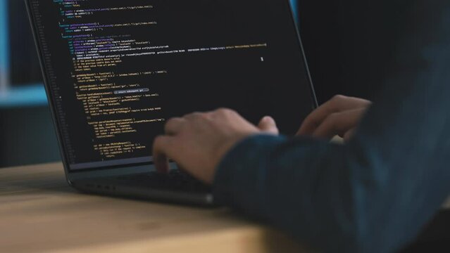Man in denim shirt coding on laptop, screen full of code in real time