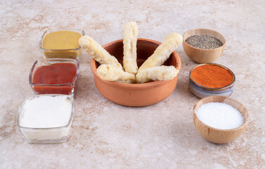 Chicken nuggets and cheese sticks on a wooden board with variety of sauces around