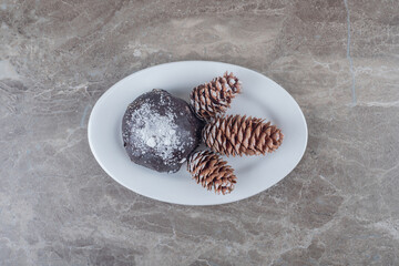 Chocolate coated cake and three pine cones on a platter on marble background