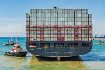 Containerschiff mit Schleppdampfern im Hafen