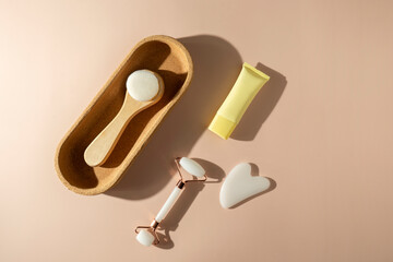 A face roller and quartz massager in the form of the heart, a face brush lying on the beige background