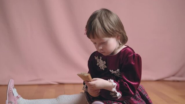 Cute little girl in an vintage burgundy dress is playing with a wooden fan. The concept of children theater productions and developing acting circles. Coral background