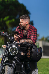 Fototapeta na wymiar Chico con camisa a cuadros roja posando con telefono movil en su motocicleta
