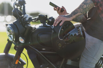 Chico atractivo tatuado en motocicleta con smartphone y gafas de sol