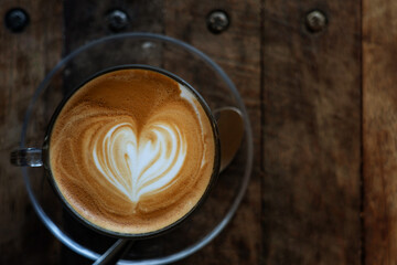 Heart shape of latte art coffee in clear cup on old wooden loft style desk , soft focus with dark tone