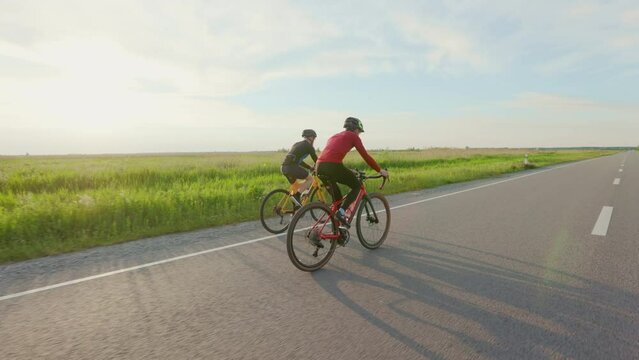 Caucasian racing bicyclists riding during intensive training along paved road. Two men in activewear and helmets preparing for cycling international competitions.