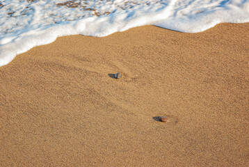 White sea foam, sandy shore, pebbles on a sandy beach. Calm inspiring sea view.