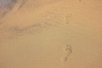 Fototapeta na wymiar Human footprints walking along the coast. Clear traces of bare human feet on the sand.
