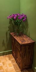 Lily flowers bouquet on vintage wooden chest of drawers in olive color painted room. Rustic interior ideas concept. Lifestyle background.