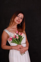 Portrait of beautiful woman in white dress with a bouquet of tulips on black background