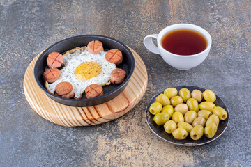 Fried egg with sausages in a black pan with a cup of tea