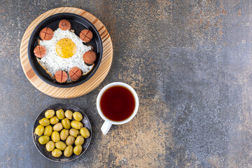 Fried egg and sausages in a pan served with olive and tea