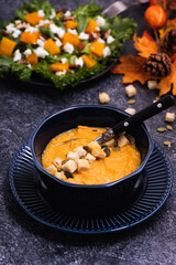 Bowl of pumpkin soup with croutons and seeds on stone kitchen counter. Copy space for your text