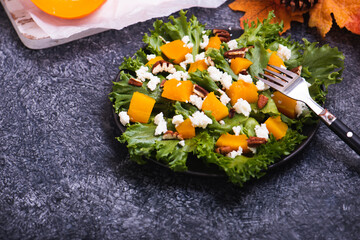 Roasted pumpkin and feta salad with olive oil and balsamic dressing. Vegetarian dinner with lettuce and walnut in a plate on stone table