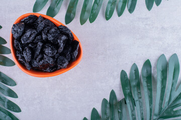 Black dry plums in a cup on concrete background