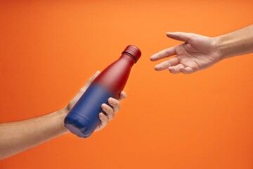 Close-up of male hands, sharing a red and blue gradient reusable steel eco thermo water bottle.
