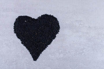 Black cumin seeds in heart shape on concrete background