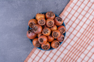 Medlars on a blue platter on grey background