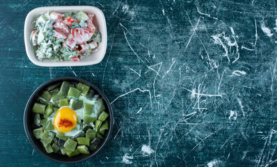 Vegetable salad with sour cream in a white plate served with fried egg and beans