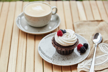 Creamy tender berries cupcake with cup of cappuccino outside. Atmospheric cozy lunch at the terrace