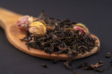 aromatic black dry tea with rose flowers on a wooden spoon isolated on black background