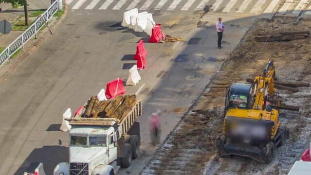 Industrial truck loader excavator moving soil and loading old railway sleepers into a dumper truck timelapse on road construction site. Aerial view of reconstruction of tram tracks on intersection